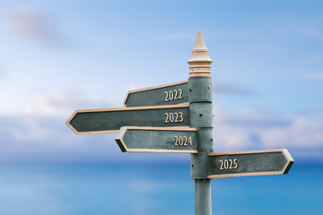 2022 2023 2024 2025 four word quote written on fancy steel signpost outdoors by the sea. Soft Blue ocean bokeh background.