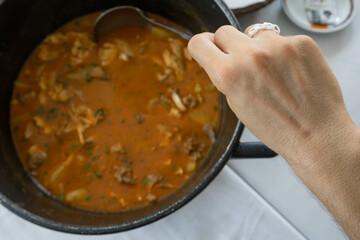 Cod stew with parsley, potatoes, and some broth in a black iron cooking pot and a man hand with a...