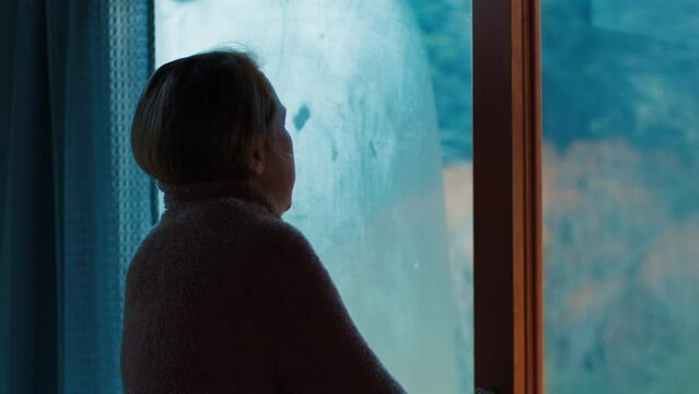 Warm blanket. Woman stands in the cold room near the window and covers herself with warm blanket