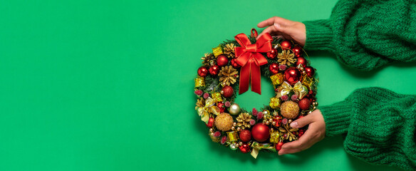 Christmas fir wreath with festive decor in female hands on green background