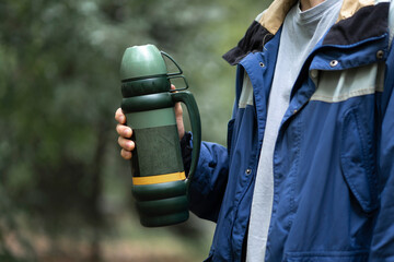 person holding a metal thermos with hot water outdoors