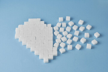 Cukier w kostkach ułożony w rozpadające się serce na niebieskim tle