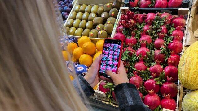 Woman photographing pomegranates on smartphone on the market. girl making photo of fruits at the store. Female Food blogger using mobile phone shoot in slow motion. 