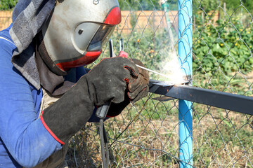 Worker welds metal pipes with electrode welding outdoors