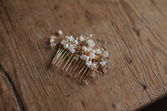 A delicate bridal hair comb adorned with pearls and floral details placed on a rustic wooden table.