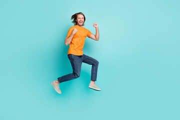Fototapeta na wymiar Full length photo of attractive lucky guy dressed orange t-shirt jumping high empty space isolated teal color background