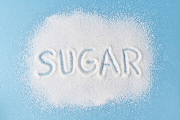 Rozsypany cukier na niebieskim tle z napisem SUGAR