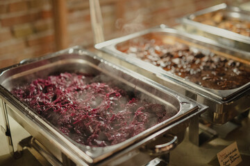 A buffet with steaming hot dishes, featuring red cabbage and meat stew in stainless steel trays, ideal for catering, weddings, and events.