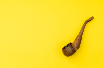 Wooden smoking pipe with tobacco on a yellow background, smoking harms