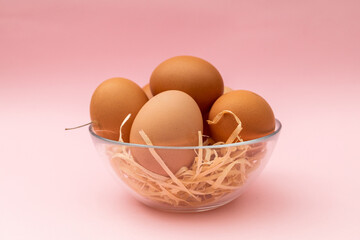 Chicken eggs in a transparent plate on a pink background