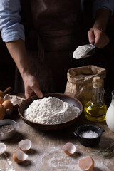 Man making bread holding scoop flour for dough and bakery ingredients for homemade cooking on table