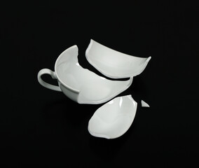 Broken white cup on black Background. An empty cup is broken into pieces.Broken Cup.	