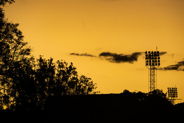 End of the day and in the distance, in the lower right corner, the silhouette of lighting equipment of a football field, in the left side the silhouette of a tree.
