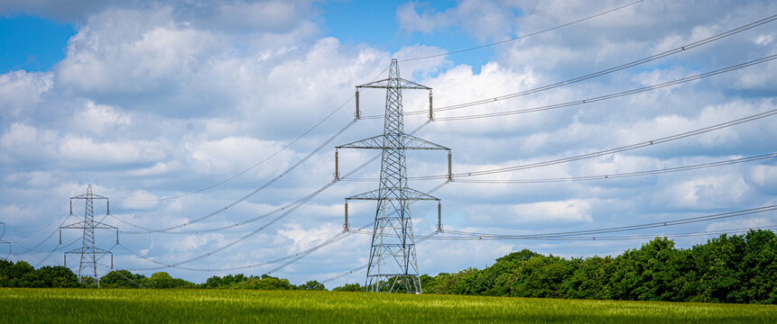 Pylon Power Electricity Electrical Distribution Aerial Cable Running through Countryside Farmer Fields with Blue Sky and White Clouds