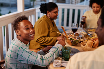 Side view portrait of smiling African American boy enjoying dinner with family on terrace outdoors