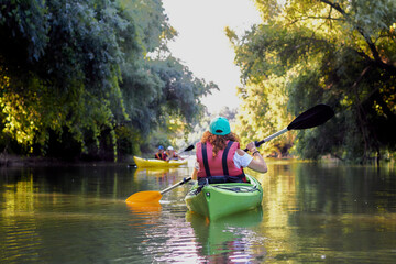 Back view of a woman rowing in a green kayak in a morning Danube river near green trees