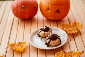 Funny spiders cookies with Halloween pumpkin among fall leaves