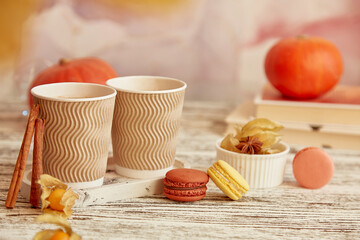 Aesthetics cardboard cups with pumpkin latte and cinnamon sticks. Seasonal coffee time with macaroons among pumpkins. Cozy autumn atmosphere