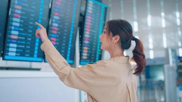 Happy asian woman traveler checking flight schedule board in airport terminal. Tourist journey trip concept