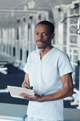 Portrait of African young therapist looking at camera while filling patient card at sport club