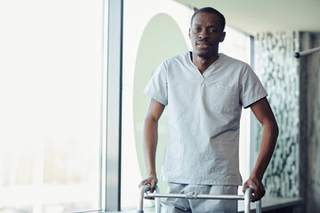 Portrait of African young patient walking with walker along the corridor at hospital