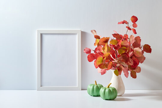 Mockup with a white frame and colorful autumn leaves in a vase, pumpkins on a light background. Empty poster frame mockup for presentation design, text, lettering