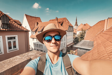 Happy man tourist with backpack taking selfie photo and enjoying panorama from the viewpoint of the orange roofs of the old town of Osnabruck in Germany
