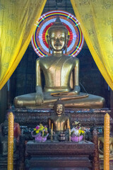 A golden Buddha statue sitting in a room with a yellow curtain - Cambodia