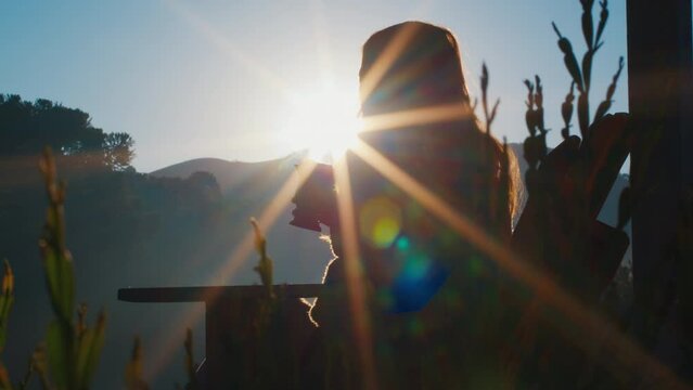 Woman drinks mate tea and enjoys sunrise in Brazilian mountains from the wooden terrace