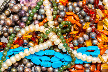 Beads and necklaces made of colored semi precious stones. Background from a variety of beautiful jewelry, multi-colored turquoise stones, amber, cat's eye, pearls.