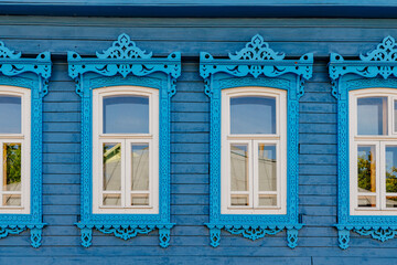 Old wooden blue windows with carved architraves. Log facade of a typical rural house. Architecture...