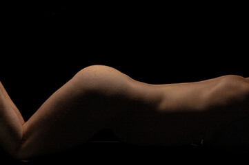 Artistic nude male fitness model with lighting on bare skin from back to thighs against black background