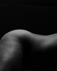 Artistic nude male model with lighting on bare skin of hips and leg with black background