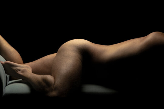young adult nude male fitness model in horizontal laying pose against black background