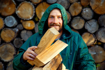 Portrait of a man with a bunch of chopped firewood. Bearded lumberjack with firewood for the fireplace. The concept of survival, recreation, country pastime.