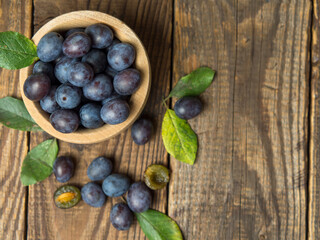 Blue plum in a bowl on a wooden table. Fruit background with copy space.