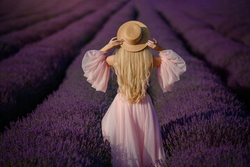 Young beautiful woman in a pink dress and a hat is walking in the lavender field.