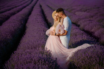 Fototapeta na wymiar a woman in a pink dress and hat and a man in a white shirt are walking in a lavender field..