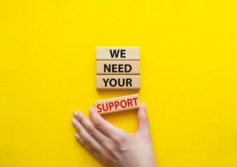 We need your support symbol. Wooden blocks with words We need your support. Beautiful yellow background. Businessman hand. Business and We need your support concept. Copy space.