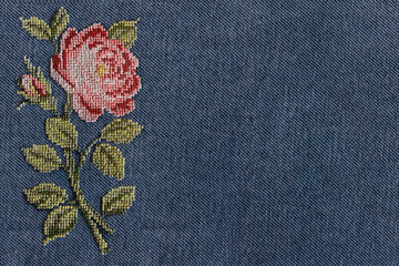 abstract background cross-stitched pink rose on the background texture blue denim fabric closeup - obrazy, fototapety, plakaty