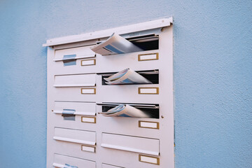 The mailbox of a residential building with daily newspapers sticking out with advertisements and news.