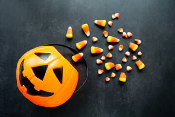 Plastic pumpkin basket with candy corn spilled out. Some of it are broken and look like small teeth. Halloween harmful sweets concept. Copy space
