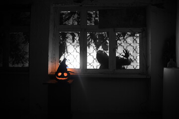 Scary Halloween pumpkin in the mystical house window at night or halloween pumpkin in night on room with blue window. Symbol of halloween in window. Selective focus