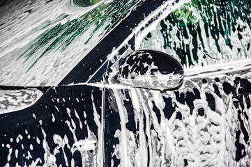 Obraz premium Hand washing the car with foam soap. The car is covered in foam.