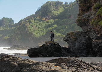 group of men standing on a black rock in a beach of the pacific ocean immerse in nature chile...