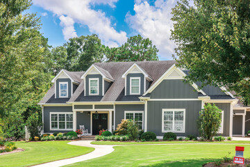 A large gray craftsman new construction house with a landscaped yard and leading pathway sidewalk