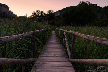 Fototapeta na wymiar Scenic view of a wooden pier on a blue lake at dawn. Reflection of mountains and water plants on water in Una, Cuenca, Spain