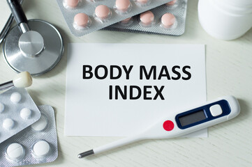 On the table a stethoscope, a pills and a white card with the text BMI Body Mass Index. View from above.