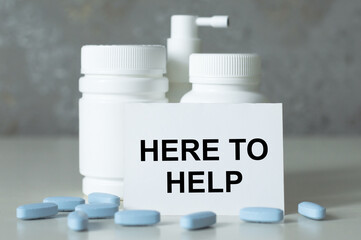 HERE TO HELP is written on a white card next to a jar of medicine and loose pills