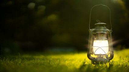 A metal kerosene lamp stands on the green grass in the garden. Lighting for the garden. A hand-held kerosene lantern.